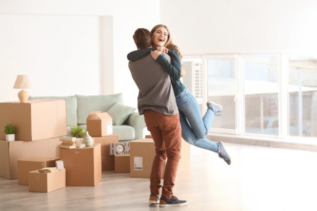 Young,Happy,Couple,In,Room,With,Moving,Boxes,At,New