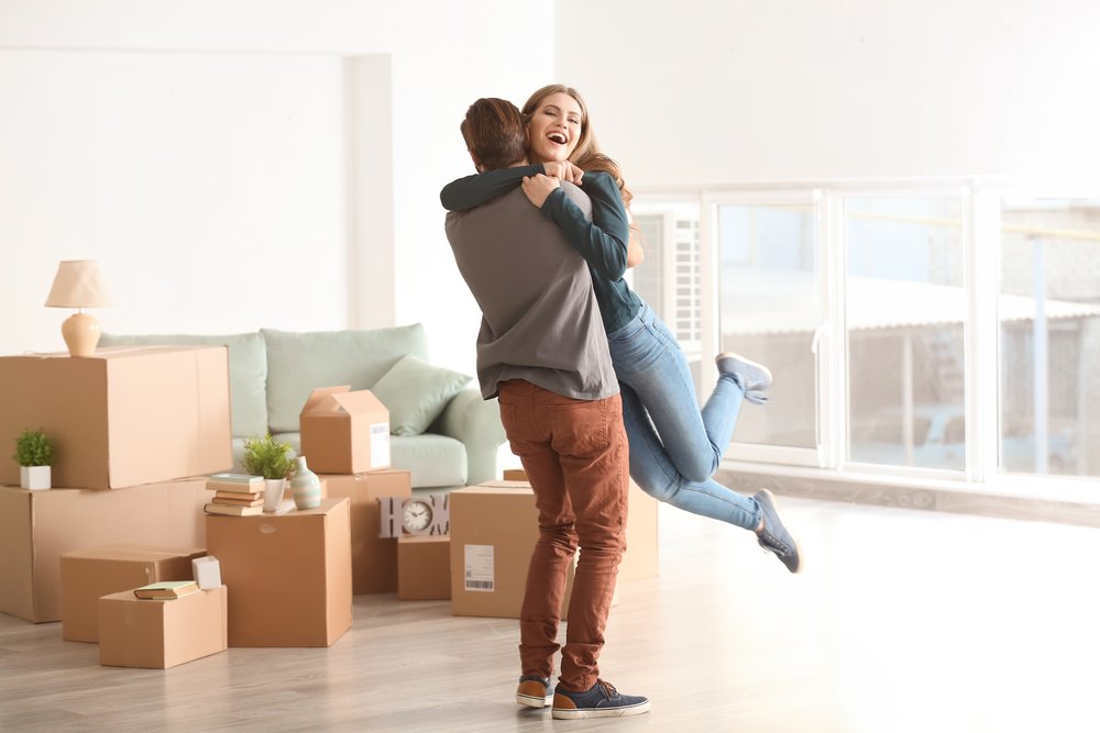 Young,Happy,Couple,In,Room,With,Moving,Boxes,At,New